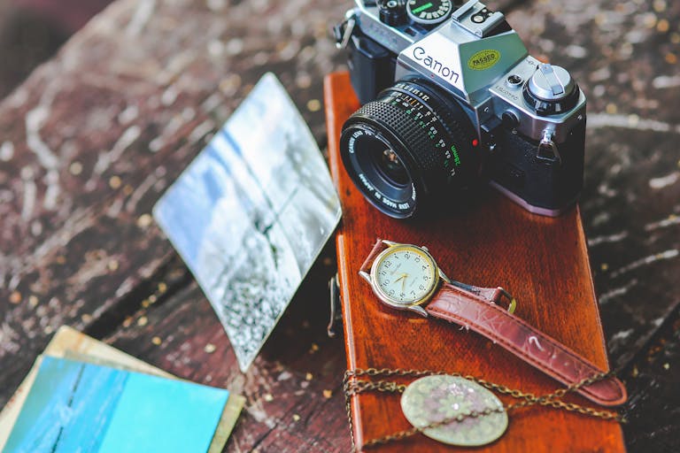 VirtusPlays Elegant composition of a vintage camera, watch, and photos on a rustic wooden table.
