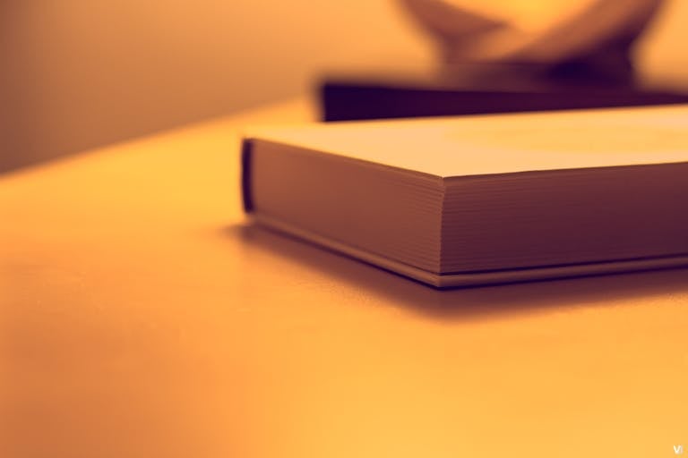 Pappedeckel: Minimalist close-up of a book on a wooden table under warm lighting, perfect for study or literature themes.