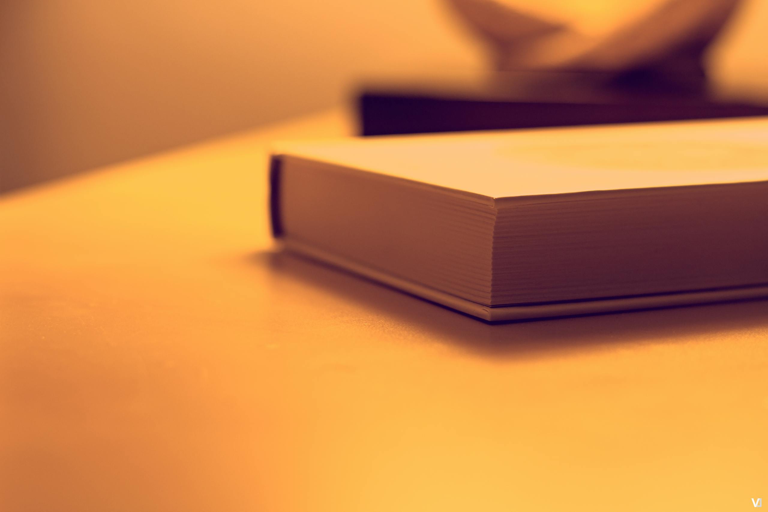 Pappedeckel: Minimalist close-up of a book on a wooden table under warm lighting, perfect for study or literature themes.