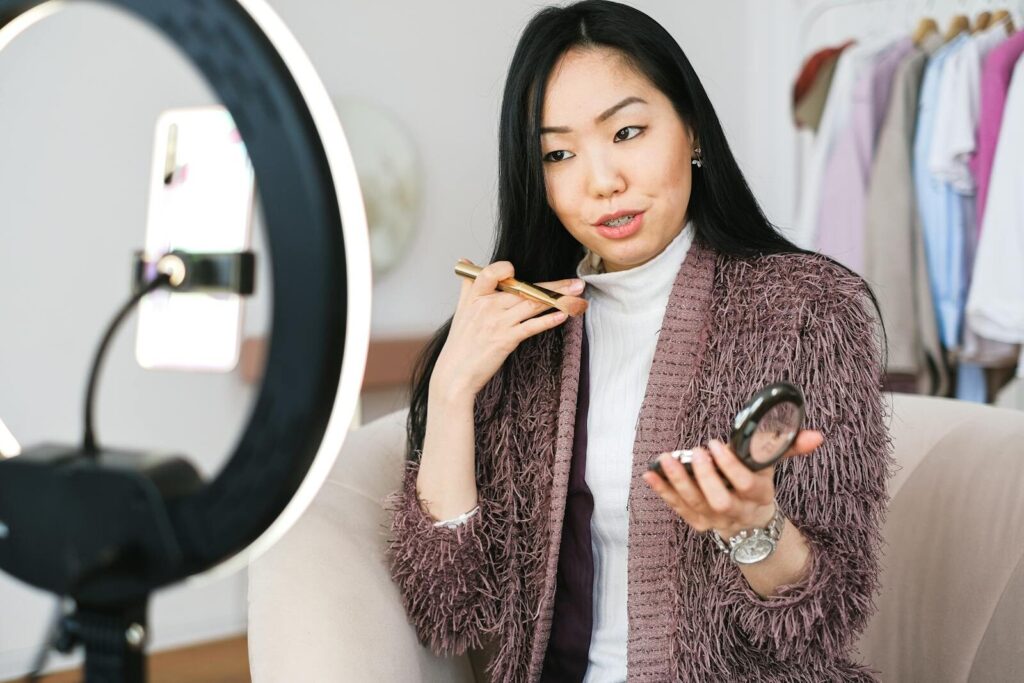 Sixmagazine Beauty vlogger demonstrating makeup tips using a ring light during live stream.