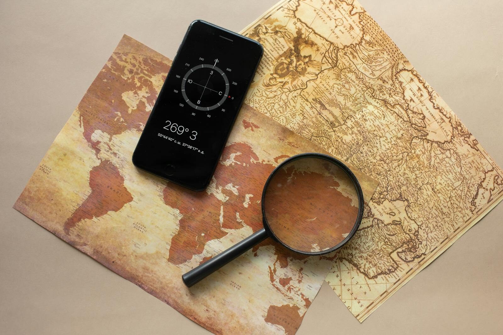 Six Sigma Certification Online Top view of magnifying glass and cellphone with compass with coordinates placed on paper maps on beige background in light room