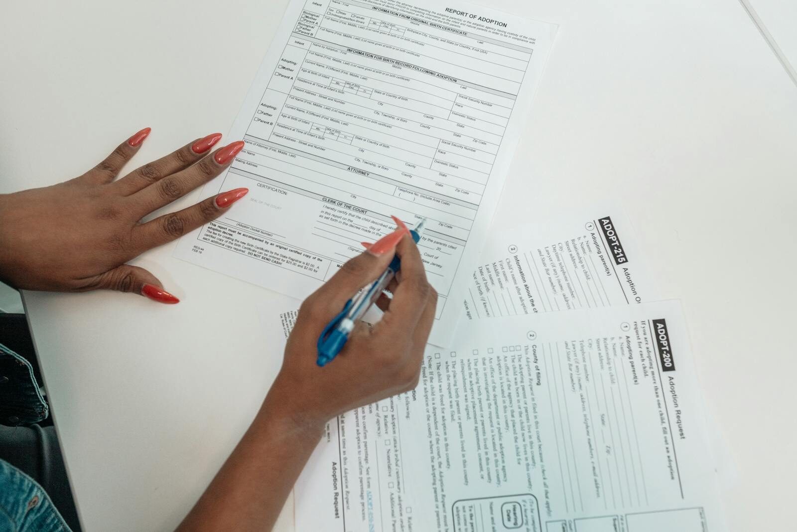 Sodiceram A woman with red nails fills out adoption application forms on a desk.