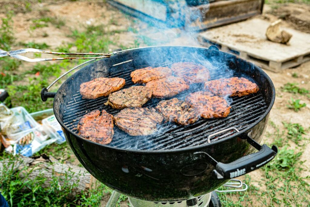 Weber Grillvorführung Grilled steaks sizzling on a charcoal grill with smoke, perfect for a summer barbecue.