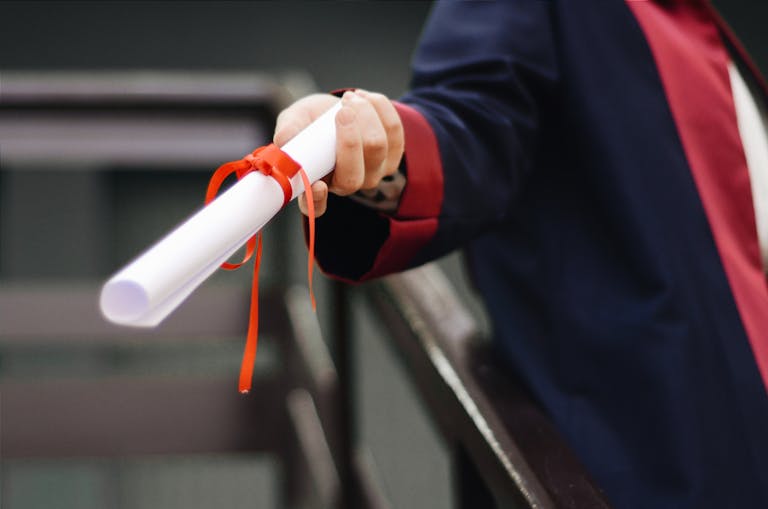 Redeepseek A close-up image of a graduate holding a diploma tied with a red ribbon, symbolizing achievement and success.