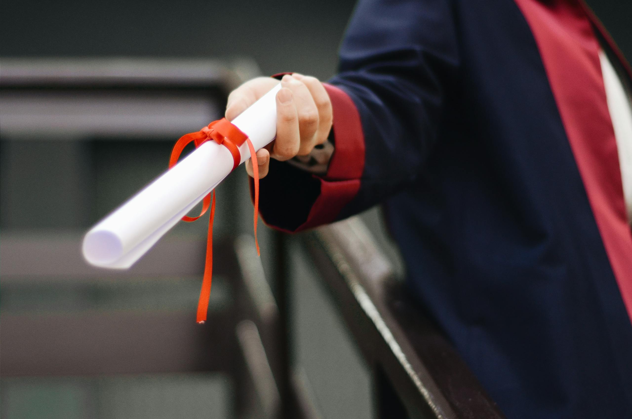 Redeepseek A close-up image of a graduate holding a diploma tied with a red ribbon, symbolizing achievement and success.