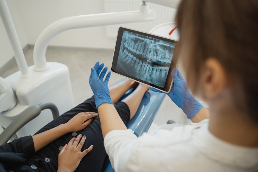 https://uitly.blog/dental-software-news-today/ A dentist showing a dental x-ray on a tablet to a patient in a clinic.