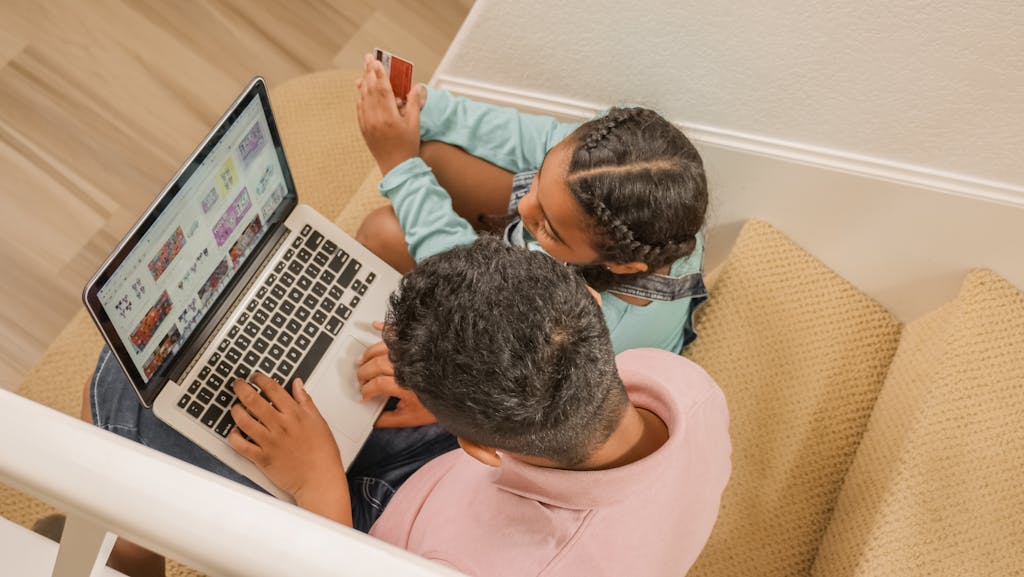 Newstook A father and daughter sit on stairs, engaging in online shopping together using a laptop.