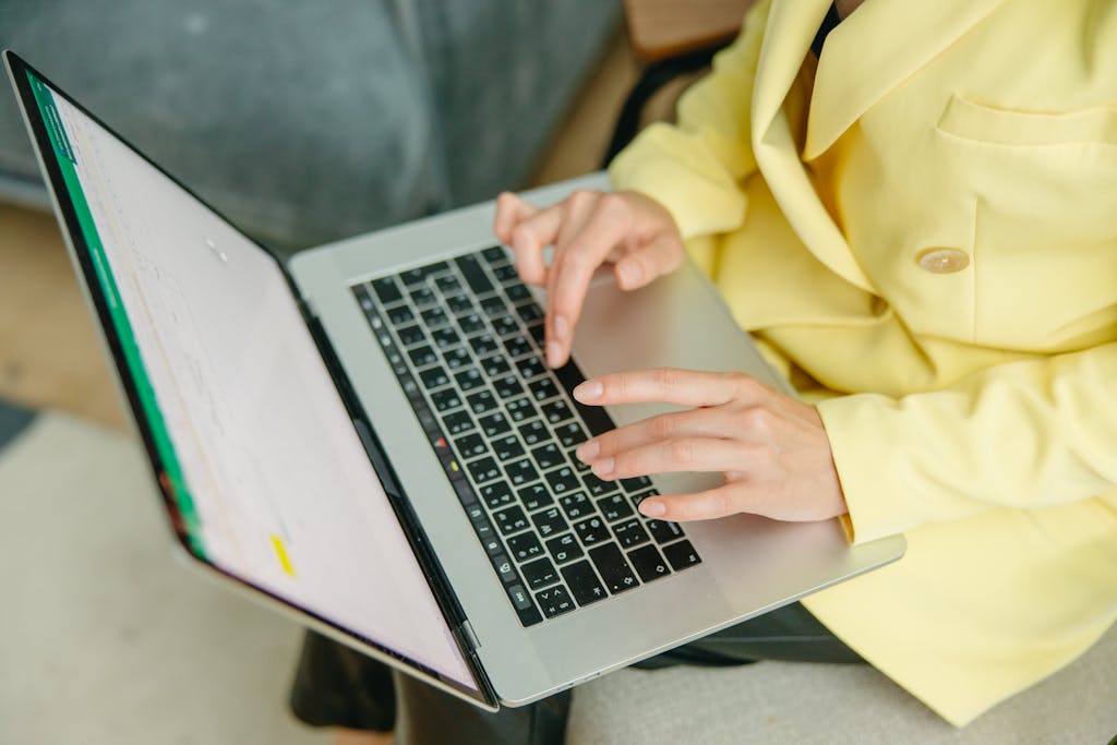 Newstook A person in a yellow jacket typing on a laptop indoors. Perfect for depicting work from home or business scenarios.
