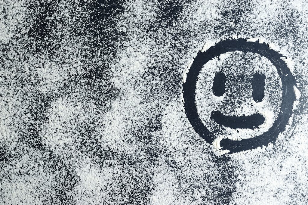 Emfyteymata  Artistic smiley face drawn through white powder on a black surface, creating an abstract texture.