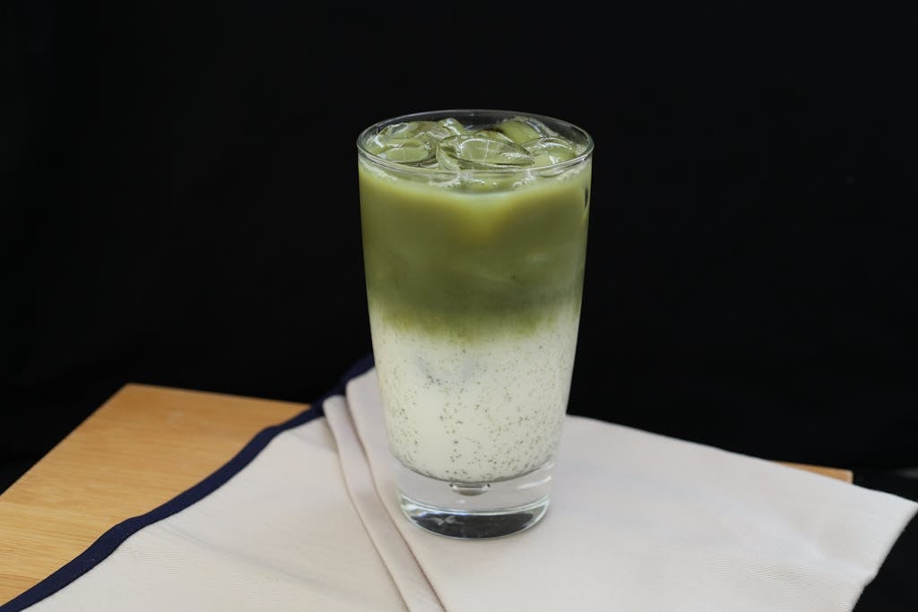 Bin Matcha Refreshing iced matcha latte in a glass with milk on a wooden table.