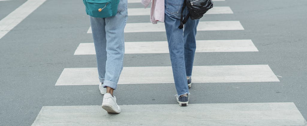 Dojen Moe Two people walking on a zebra crossing in urban setting, casual attire.