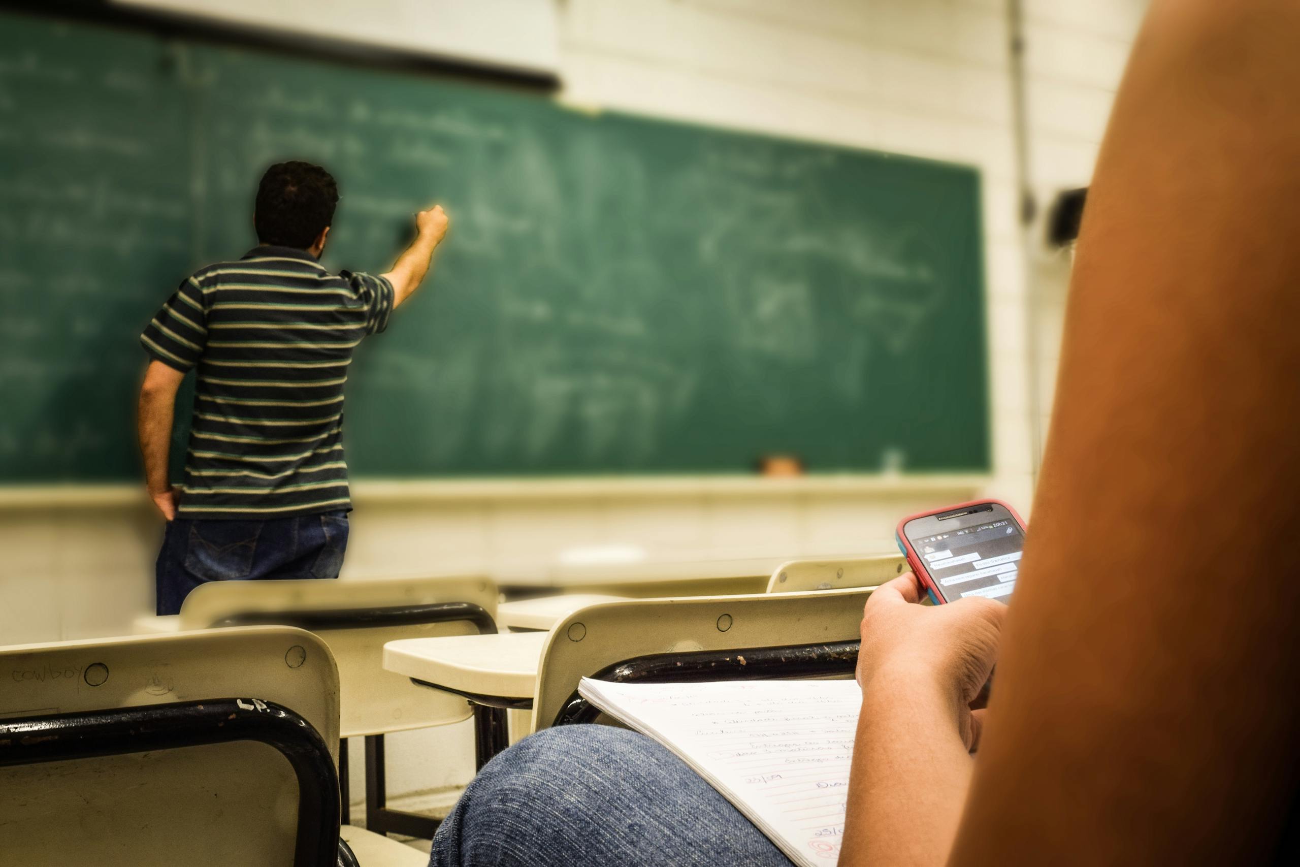 Algebra.learning Nexus.one texting in a classroom while teacher is writing on the blackboard.